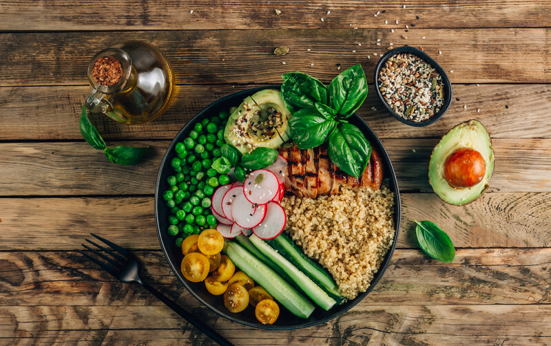 Färgglad skål med avokado, grönsaker och balanserade livsmedel på träbord